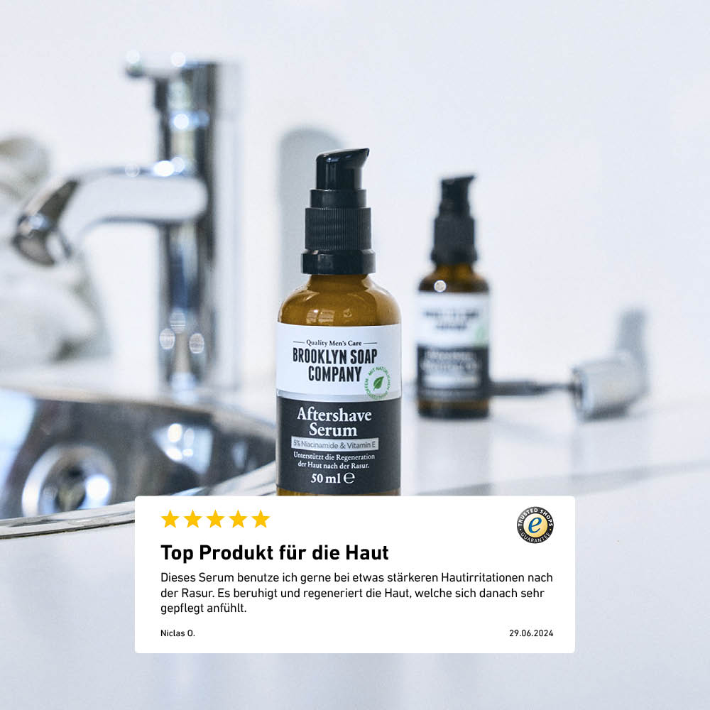 Flasche des Brooklyn Soap Company Aftershave Serums auf einem Waschbeckenrand, mit Kundenbewertung im Vordergrund über die hautberuhigende Wirkung des Produkts.