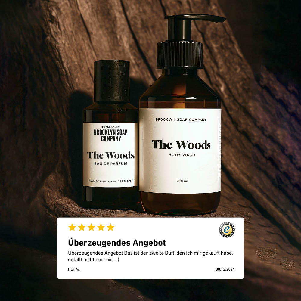 Zwei Pflegeprodukte der Brooklyn Soap Company aus der Serie "The Woods" – Eau de Parfum und Body Wash – stehen nebeneinander vor einem natürlichen Holz-Hintergrund. Im Vordergrund eine Kundenbewertung mit fünf Sternen und dem Text „Überzeugendes Angebot“.